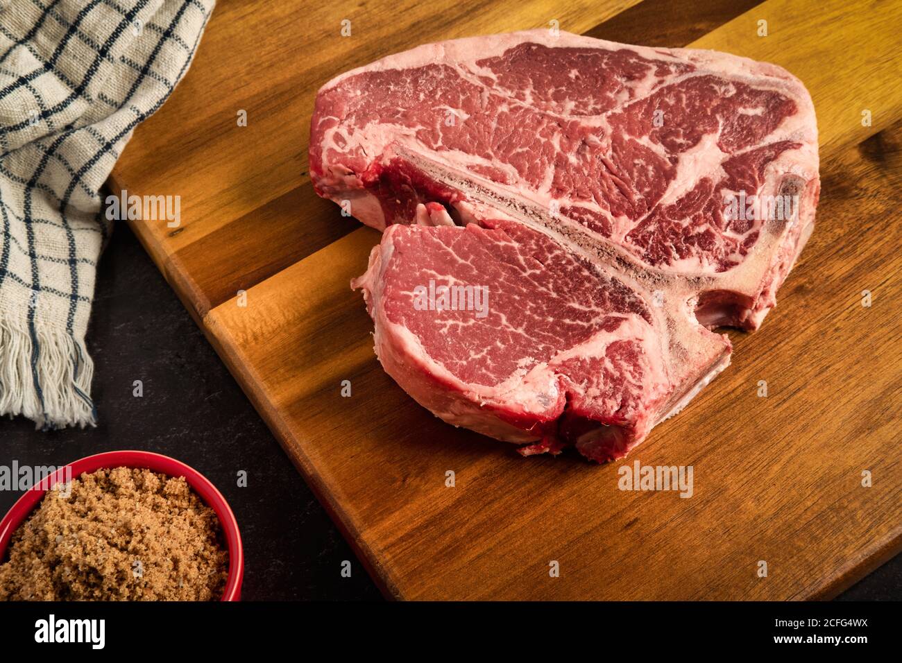 Fotografia della bistecca di Porterhouse su un tagliere, con uno strofinaccio marrone speziato sul lato, con un asciugamano da cucina sullo sfondo Foto Stock