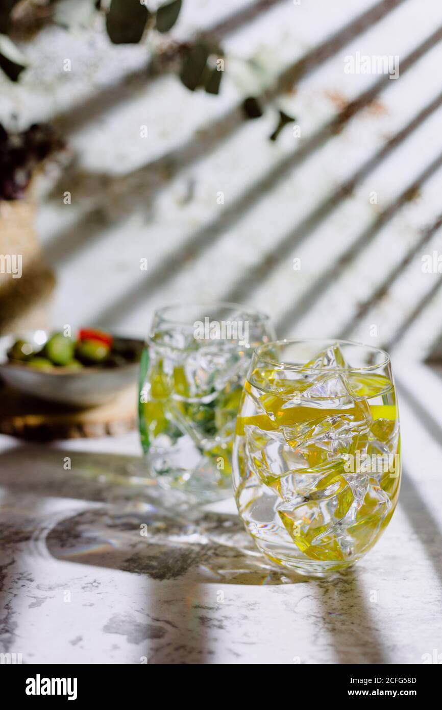 Grandi bicchieri di mojito cocktail con foglie di menta e ghiaccio cubetti  messi su superficie di calcestruzzo vicino piastra con cetrioli e. vaso con  pianta vicino parete di shabby Foto stock -