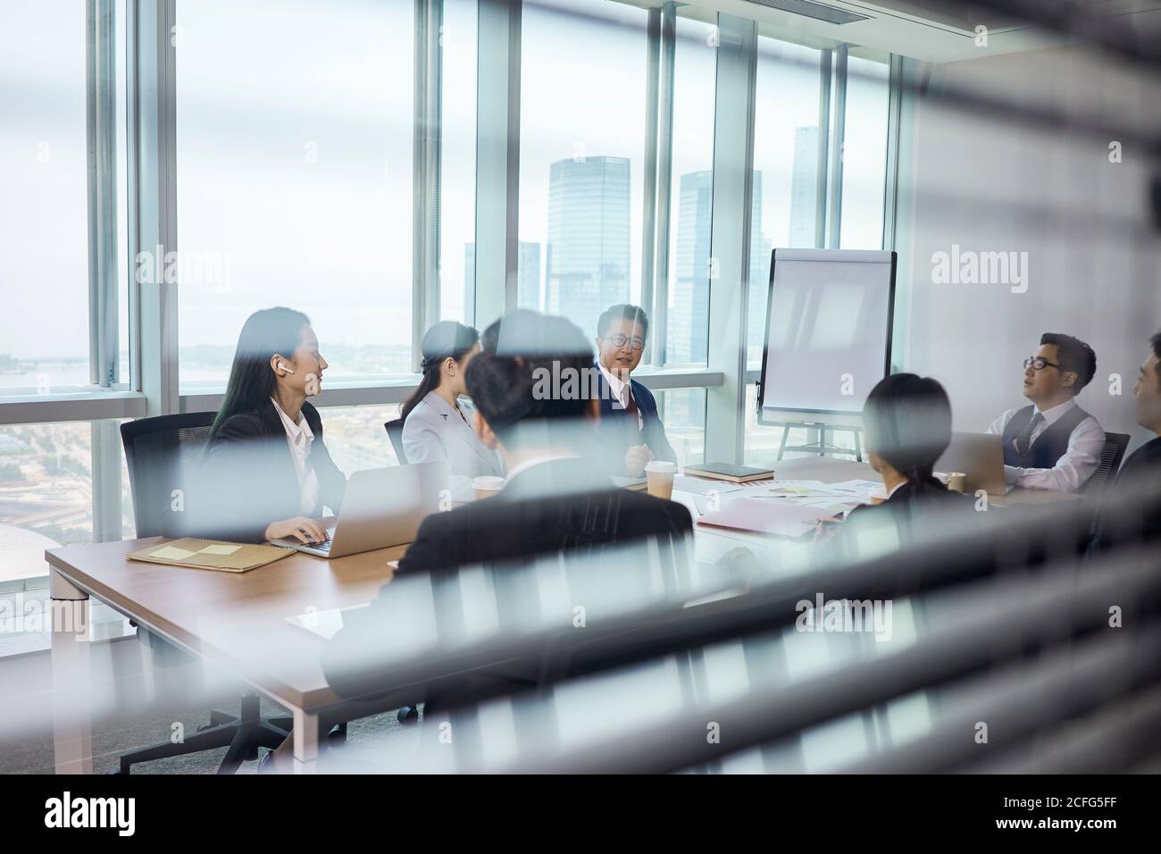 attraverso il vetro di una squadra di uomini d'affari asiatici riunione nella sala conferenze aziendale Foto Stock