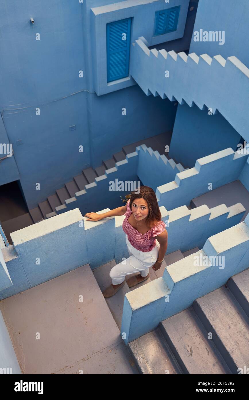 Vista dall'alto della giovane donna che cammina al piano superiore su un moderno edificio blu guardando la macchina fotografica Foto Stock