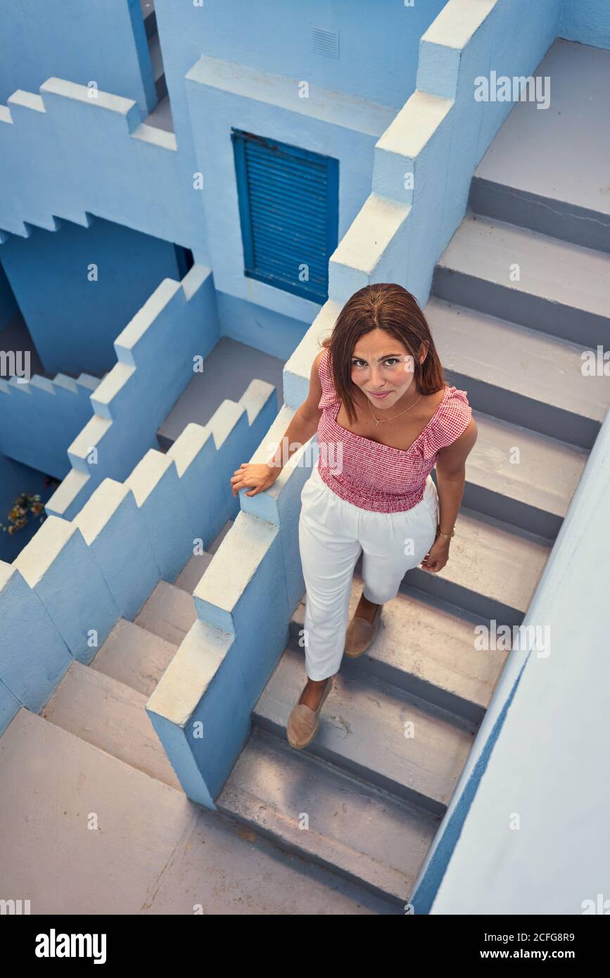 Vista dall'alto della giovane donna che cammina al piano superiore su un moderno edificio blu guardando la macchina fotografica Foto Stock