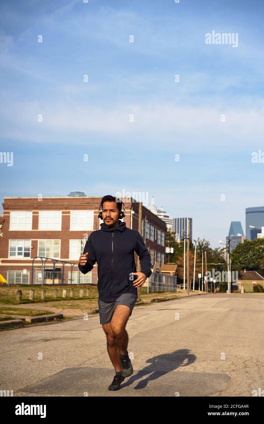 Concentrato atleta ispanico maschile in abbigliamento sportivo con cuffie in esecuzione lungo una strada vuota in centro Foto Stock