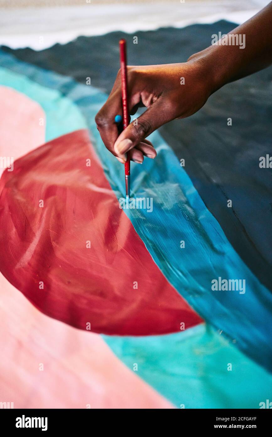 Dall'alto del raccolto anonimo nero femmina con disegno pennello immagine colorata su carta mentre si è seduti a casa Foto Stock