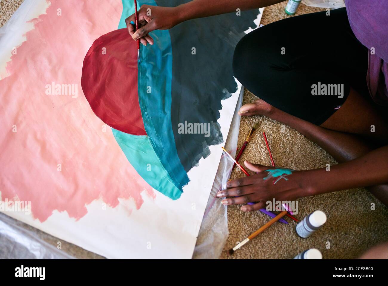 Dall'alto del raccolto anonimo nero femmina con disegno pennello immagine colorata su carta mentre si è seduti a casa Foto Stock