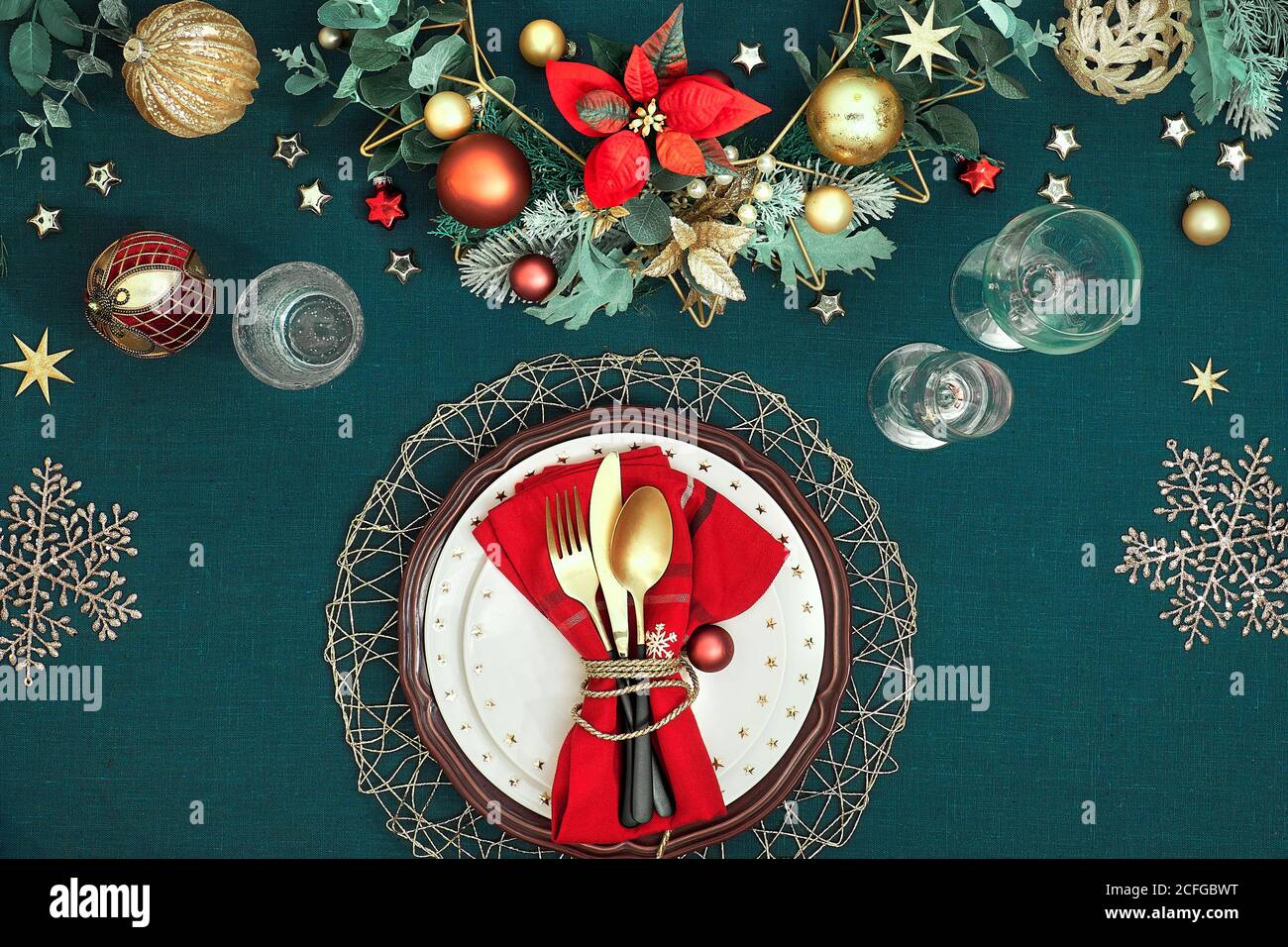 Tavolo natalizio con piatti bianchi, utensili dorati e decorazioni dorate di colore rosso scuro. Disposizione piatta, vista dall'alto su sfondo in tessuto di lino blu scuro. Foto Stock