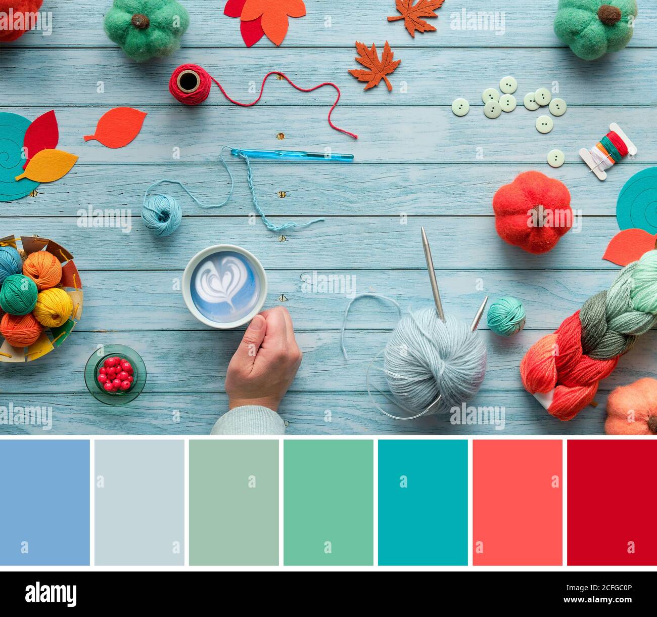 Tavolozza di colori che si abbina da autunno piatto posare su legno di menta blu. Fasci di lana, palle di filato, zucche feltrate e foglie. Per le mani, tenere la tazza con latte blu. Foto Stock
