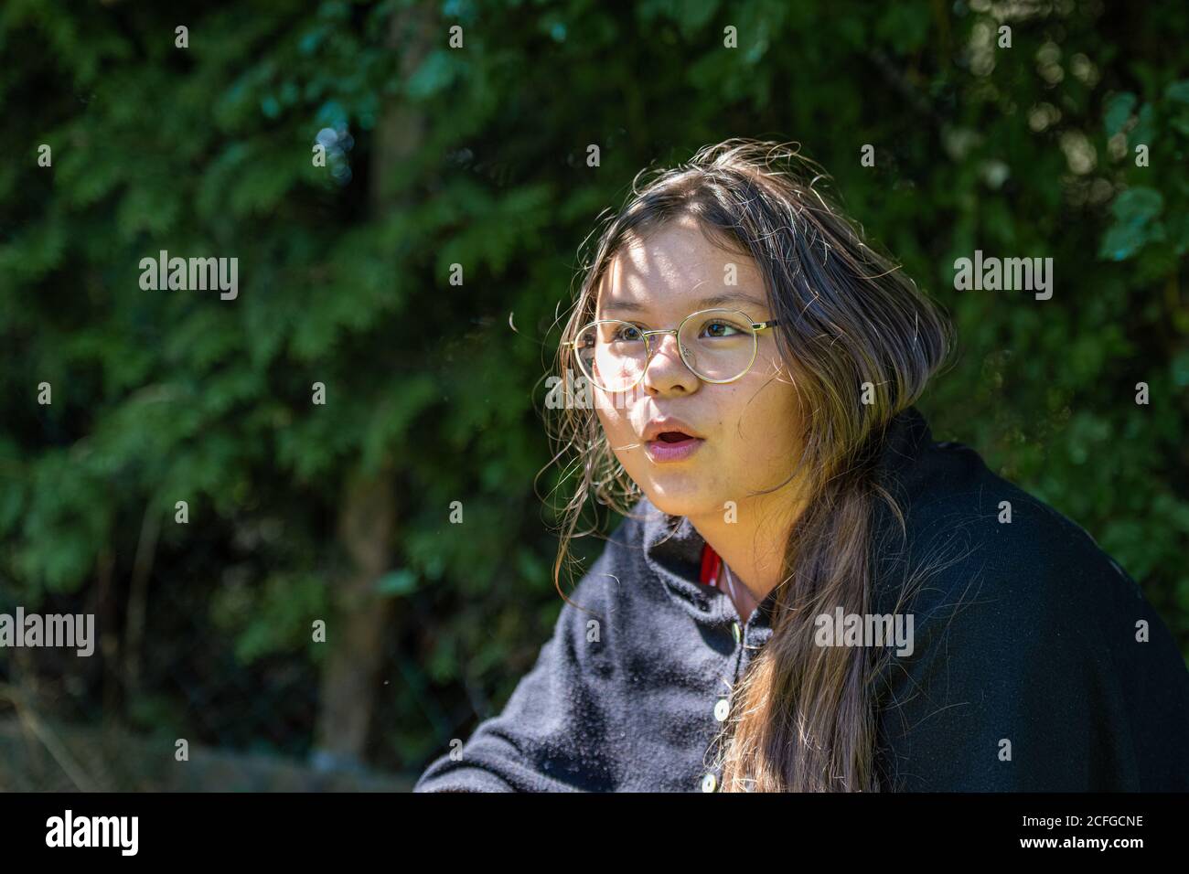 Una ragazza preteen con lunghi capelli marroni. Profondità di campo poco profonda. Sfondo verde delle foglie. Foto Stock