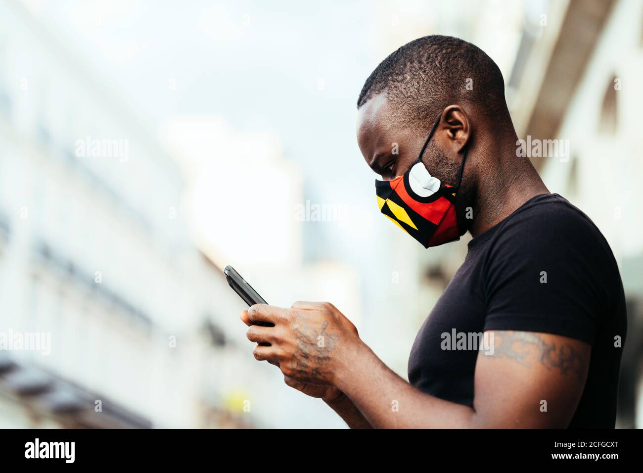 Ritratto closeup di un uomo afro-americano che indossa una maschera colorata. Sta usando un cellulare con espressione seria Foto Stock