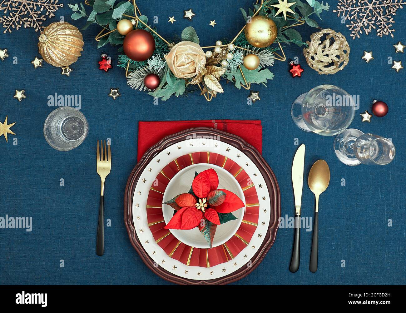 Tavolo di Natale in oro, borgogna e blu scuro. Disposizione piatta, vista dall'alto su un tavolo decorativo con posate dorate e deco tradizionale Foto Stock