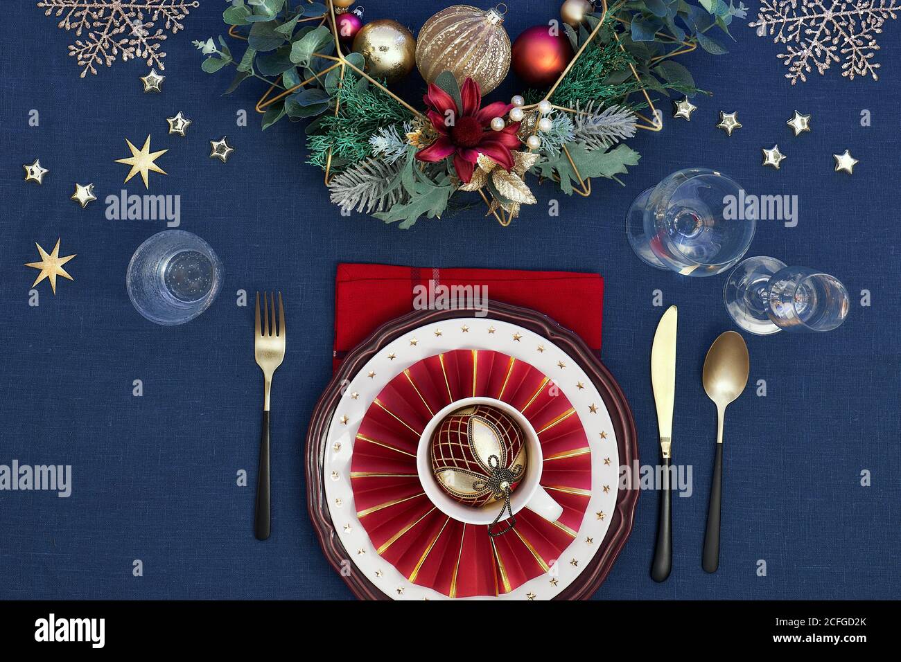 Tavolo di Natale in oro, borgogna e blu scuro. Piatto, vista dall'alto sul tavolo da pranzo con posate dorate e decorazioni natalizie Foto Stock