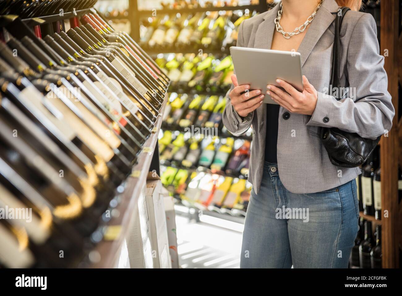 Donna d'affari senza volto in giacca grigia che tiene e naviga tablet in piedi con un amico. Foto Stock