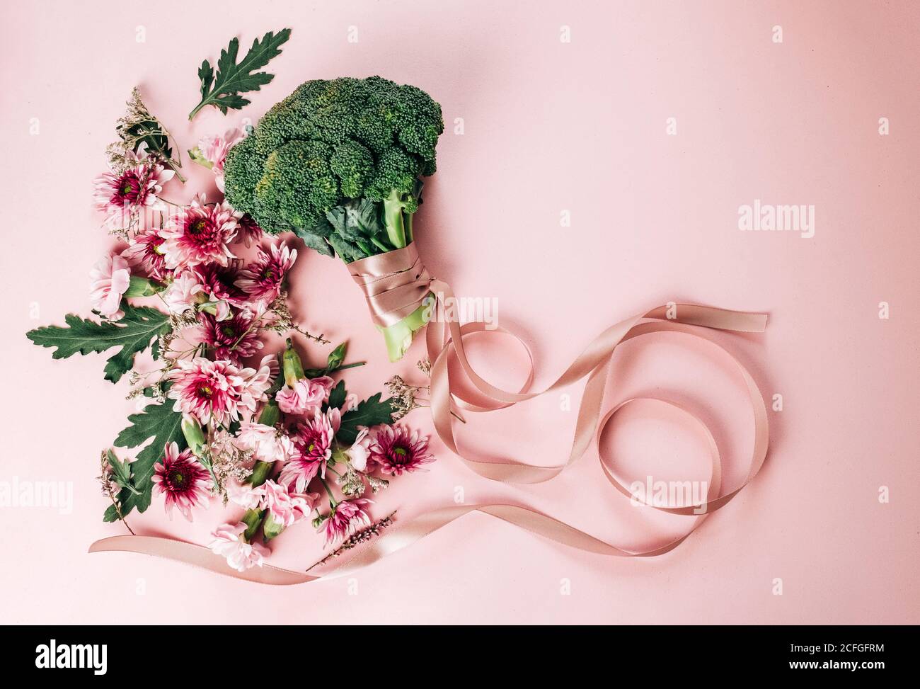 Vista dall'alto di un mazzo di fiori graziosi e broccoli maturi con nastro di seta disposto su sfondo rosa il giorno d'estate Foto Stock