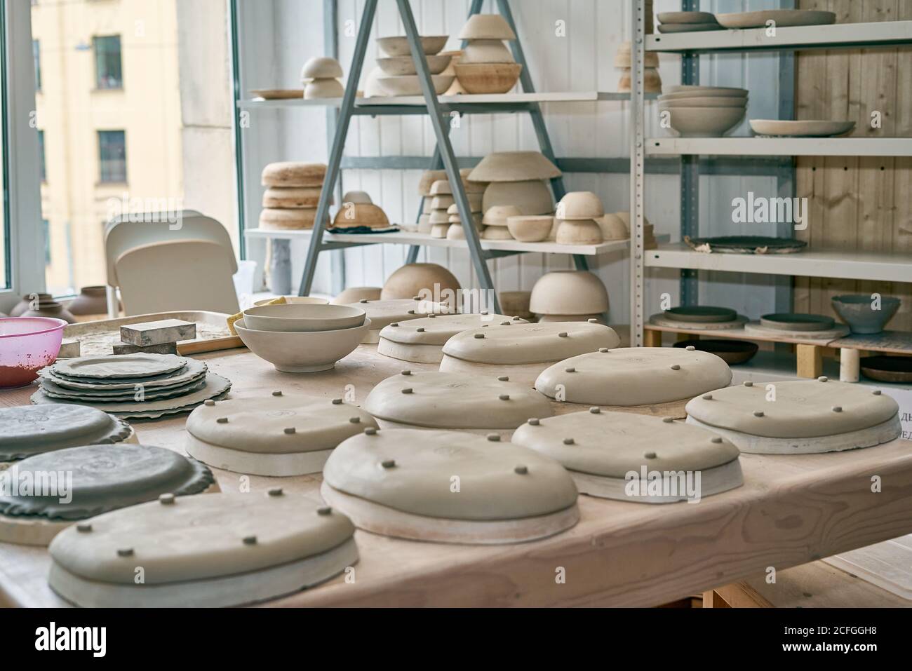 Fabbricazione di prodotti ceramici, pezzi in lavorazione. Primo piano di sfondo con pezzi di ceramica sul tavolo di oggetti contro la finestra Foto Stock