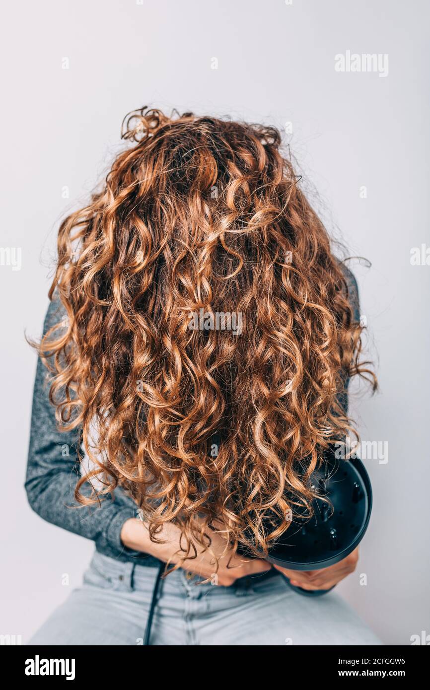 Donna seduta sulla sedia che piega i capelli ricci con asciugacapelli Foto  stock - Alamy