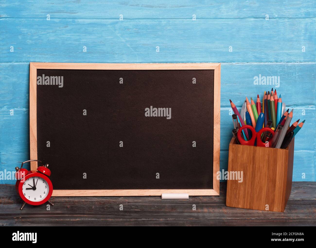 Mockup di bordo nero, matite, mantello, gessetti su sfondo di legno Foto Stock