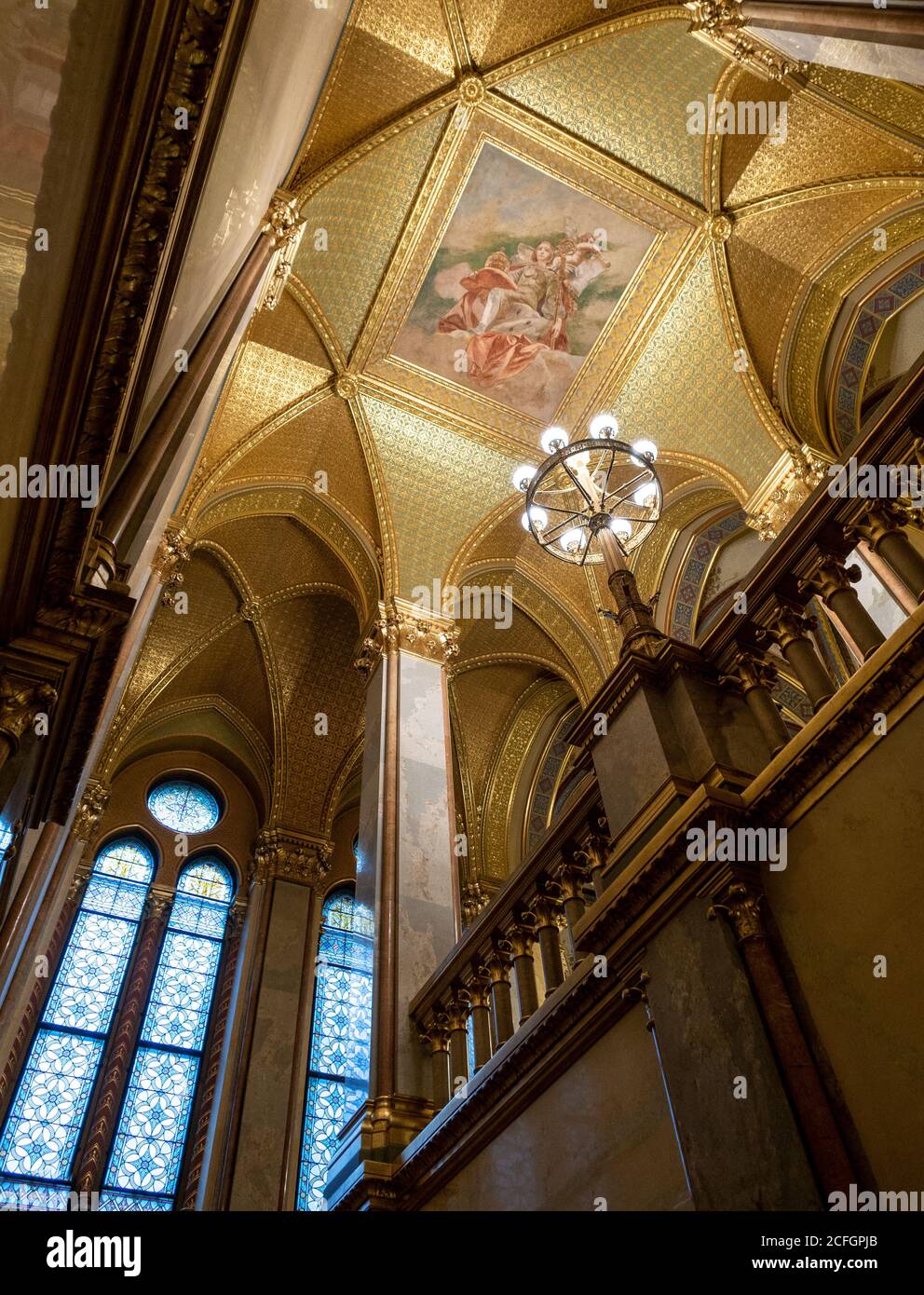 Opulento soffitto parlamentare: Una candelabra dorata illumina il soffitto dipinto incorniciato da foglie d'oro in una scala dell'edificio del Parlamento ungherese. Foto Stock