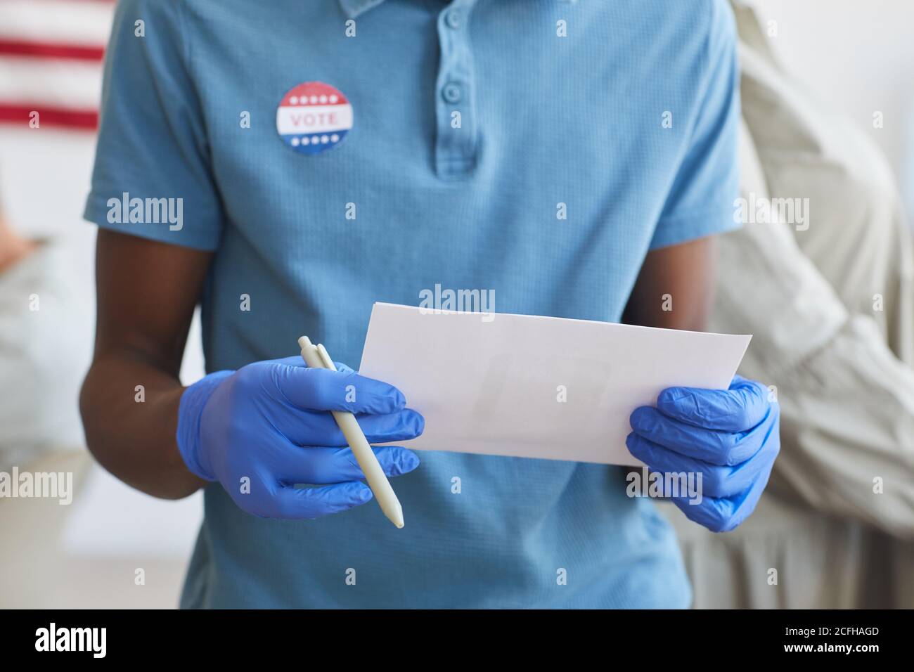 Ritratto troncato di un uomo afroamericano irriconoscibile che tiene il voto e si sta in piedi presso la cabina di voto nel giorno delle elezioni post-pandemiche, copia spazio Foto Stock