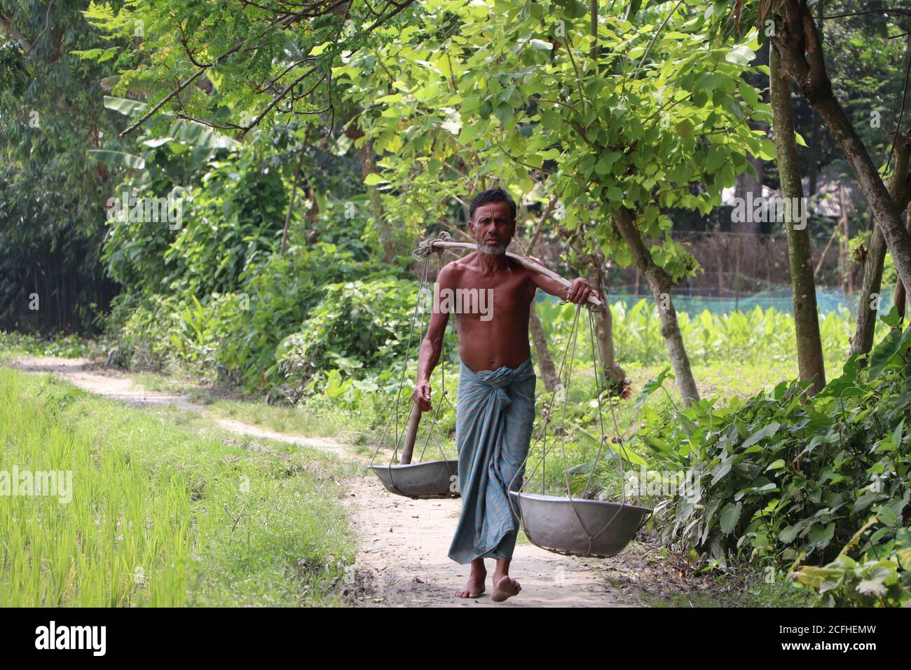 Agricoltore asiatico che trasporta attrezzi agricoli (vanga, ciotole) per lavorare nel terreno agricolo più vicino nella zona rurale di Bogura, Bangladesh Foto Stock