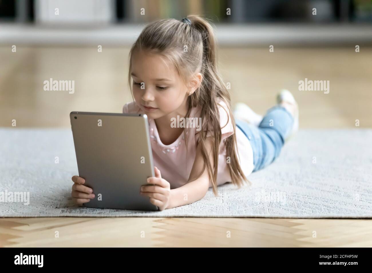 Primo piano bambina che usa un tablet per computer, sdraiata sul pavimento Foto Stock