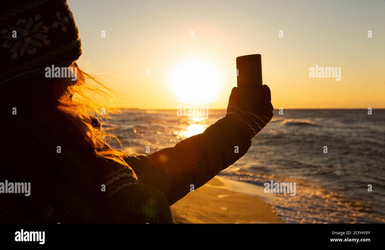Una donna che viaggia fotografa il mare all'alba con una fotocamera per smartphone. Foto Stock