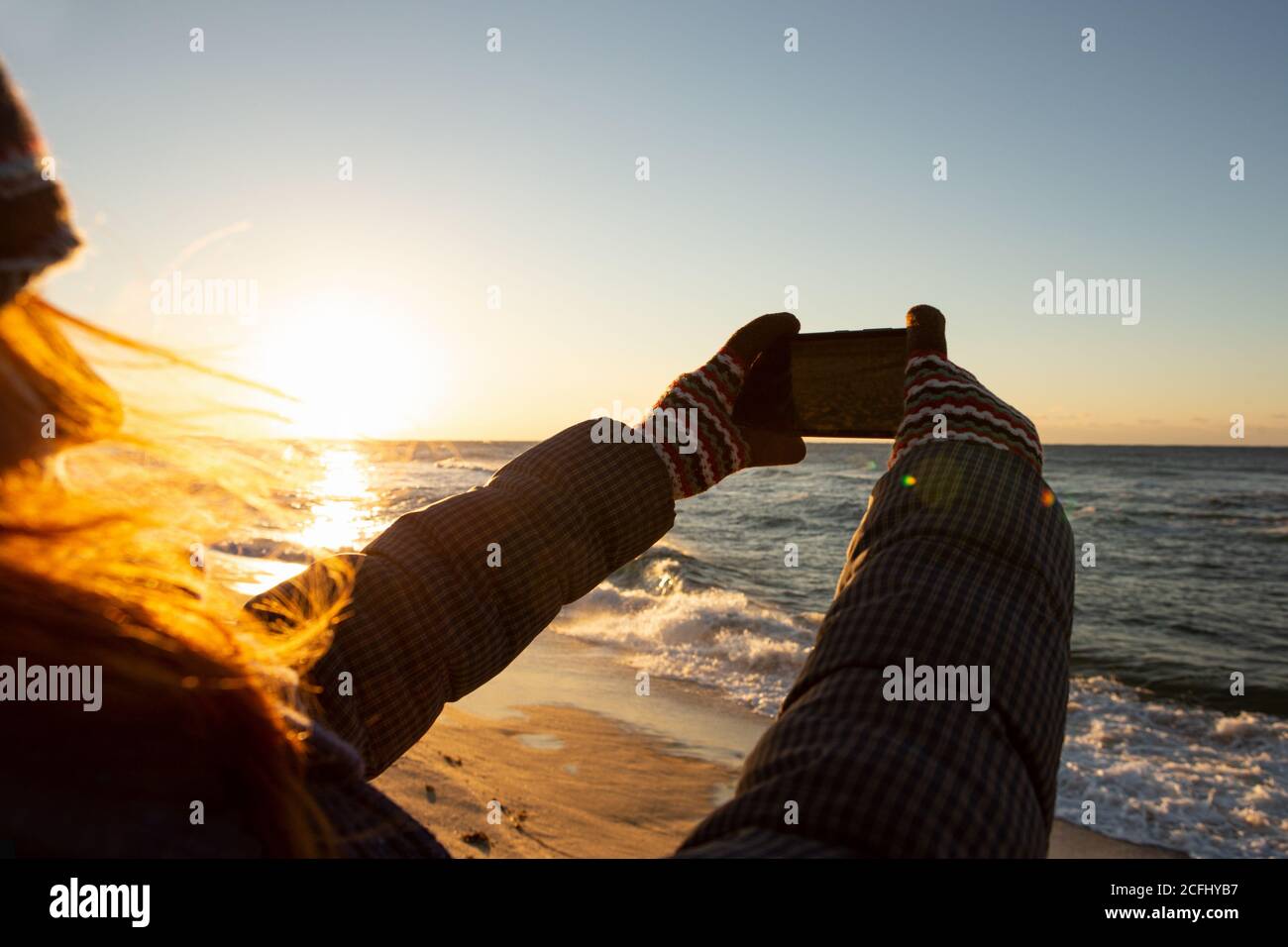 Una donna che viaggia fotografa il mare all'alba con una fotocamera per smartphone. Foto Stock
