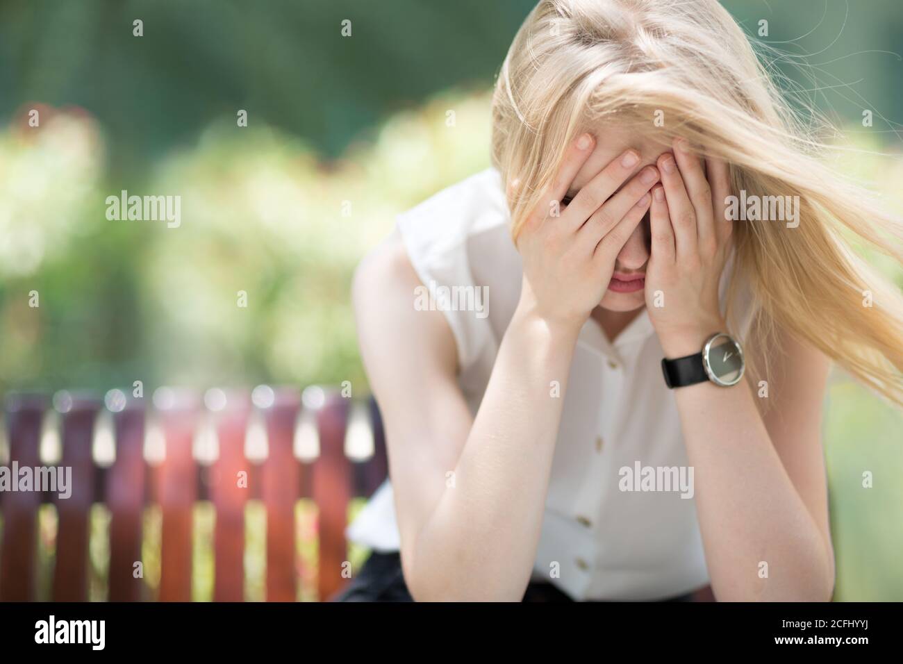 Ansia e depressione. Triste giovane donna in dolore piangendo e coprendo il suo volto mentre si siede da sola su una panchina del parco in una giornata di sole. Foto Stock