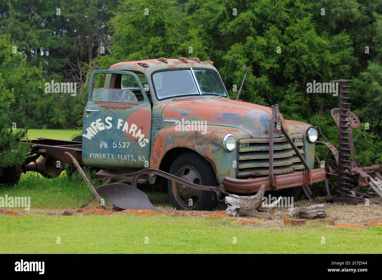 Vecchio camion agricolo Chevrolet con un aratro, falciatrice e alberi con erba fuori nel paese in Kansas. Foto Stock