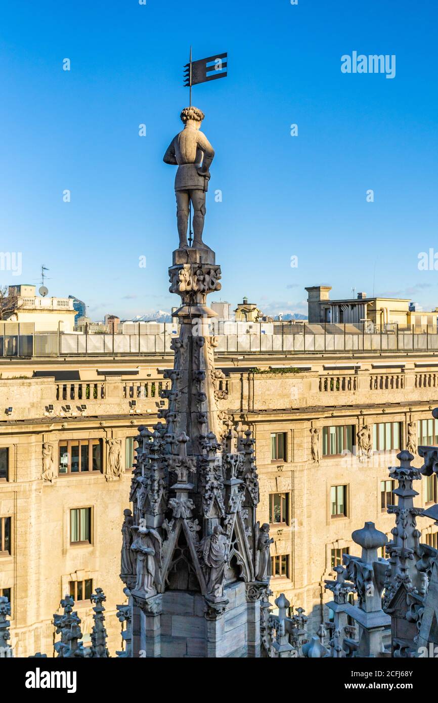 Milano, Italia - 23 dicembre 2019 - la statua di Male si erge sulla sommità di una torre del Duomo, la famosa chiesa di Milano, in Italia, su una chiara e luminosa facciata blu Foto Stock