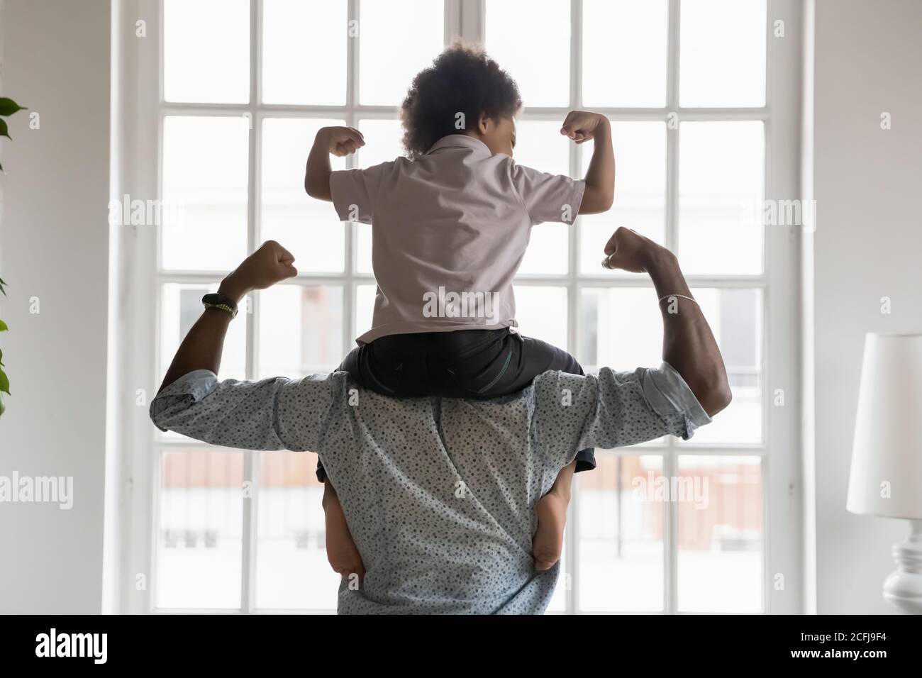 Padre afroamericano con il figlio piccolo sulle spalle che mostra i bicipiti. Foto Stock