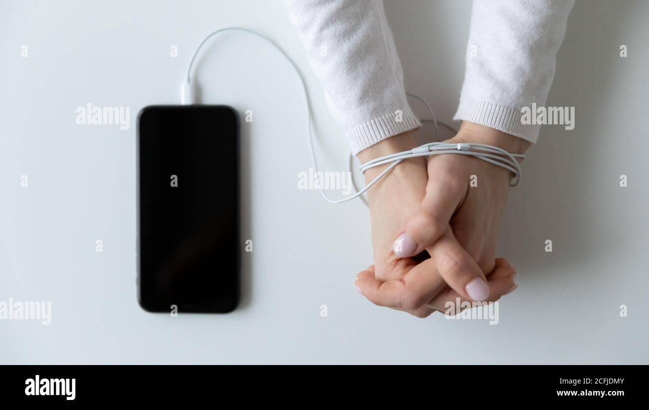 Le mani femminili sono avvolte nei cavi dello smartphone. Foto Stock