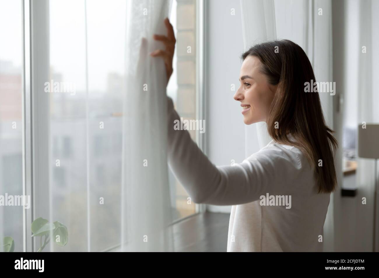 Vista laterale Felice attraente donna che apre tende. Foto Stock