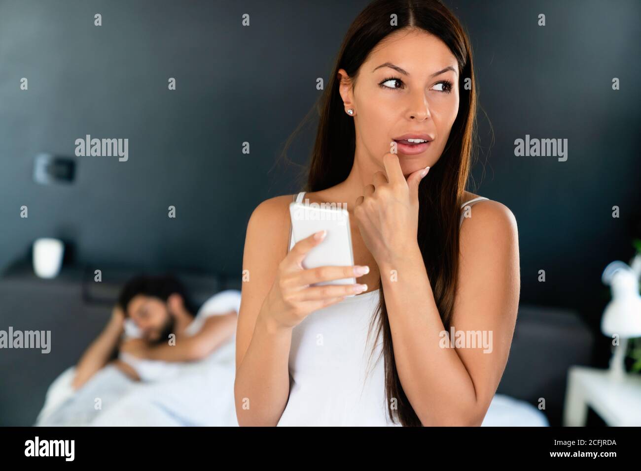 Donna che parla privatamente sul cellulare mentre suo marito dorme sopra letto Foto Stock