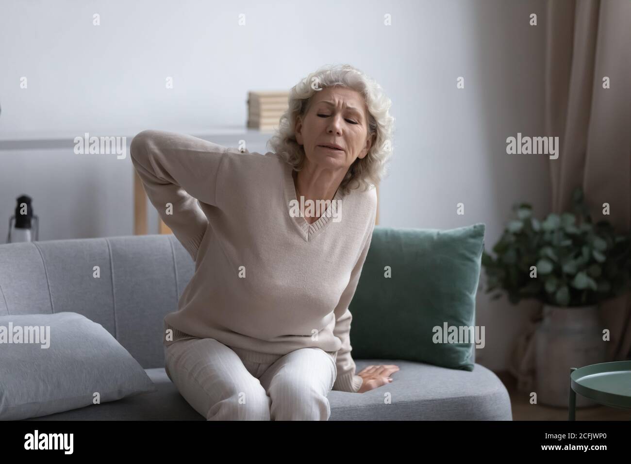 Infelice donna di mezza età che soffre di mal di schiena, seduta sul divano Foto Stock