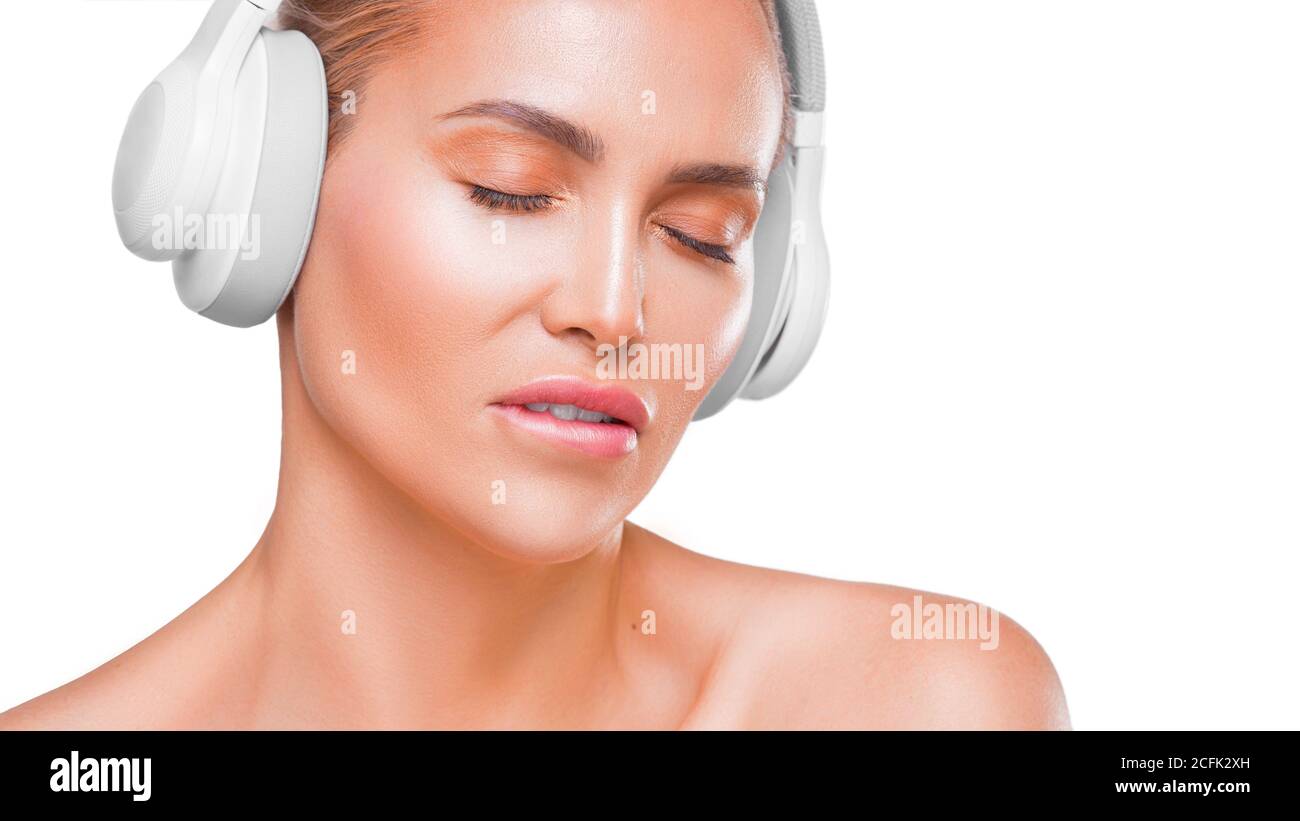 Ritratto di una bella donna in cuffia bianca che ascolta musica, punta il labbro, con occhi chiusi su sfondo bianco. Foto Stock