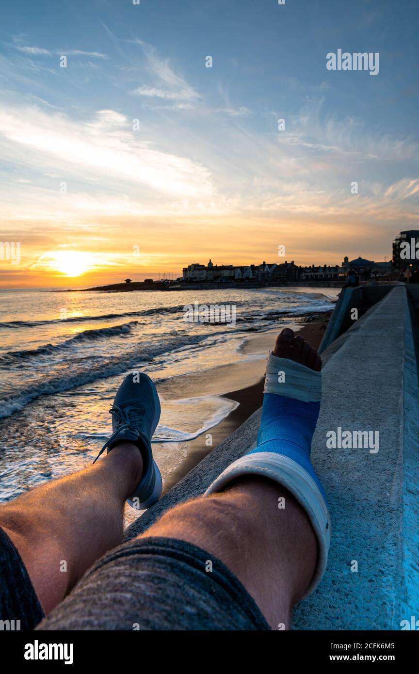 Maschio Sat sulla parete con getto a piedi godendo il tramonto al porthc awl Foto Stock