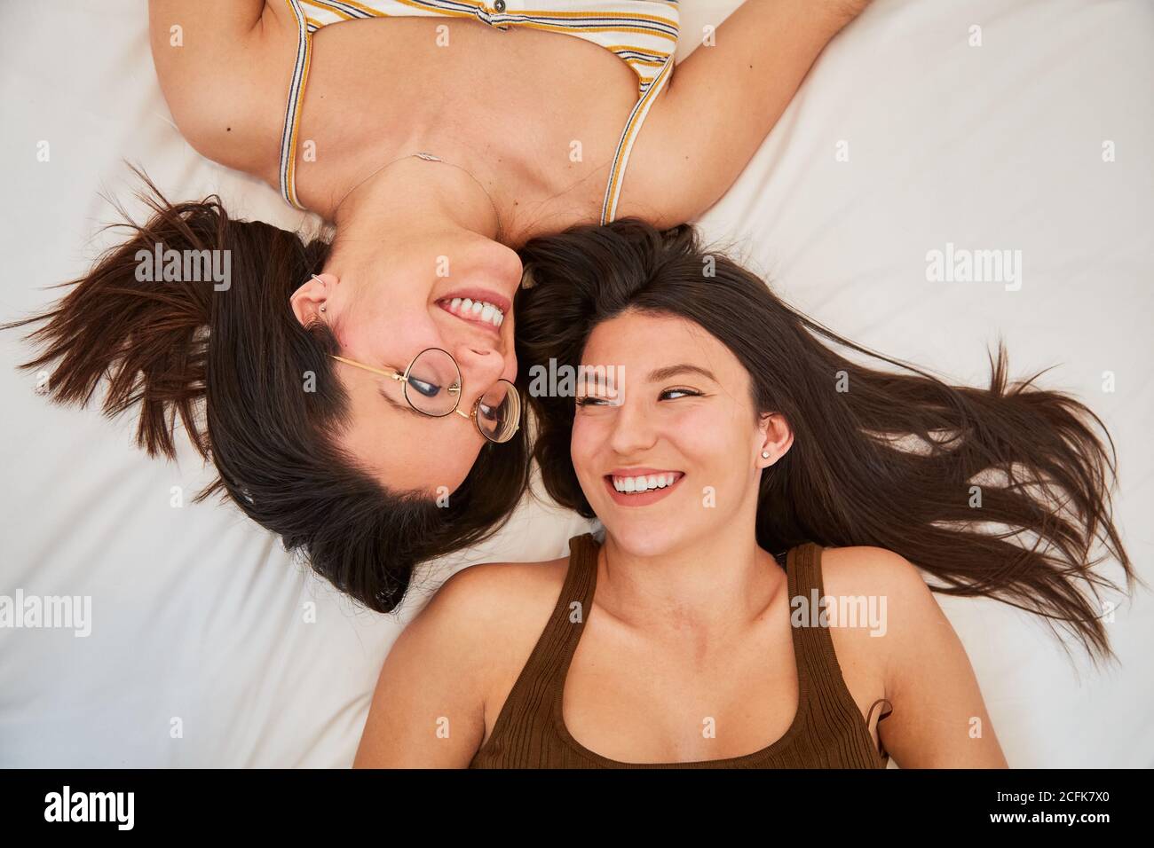 Vista dall'alto di donne amichevoli che giacciono sul viso morbido del letto per affrontare mentre si rilassa durante il fine settimana a casa e guardare l'uno all'altro Foto Stock