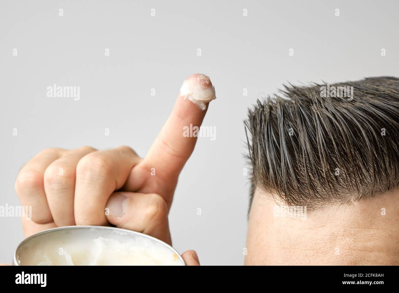 Uomo che applica una creta, una pomata, una cera, un gel o una mousse da  una scatola di metallo rotondo per lo styling dei suoi capelli dopo il  taglio dei capelli del