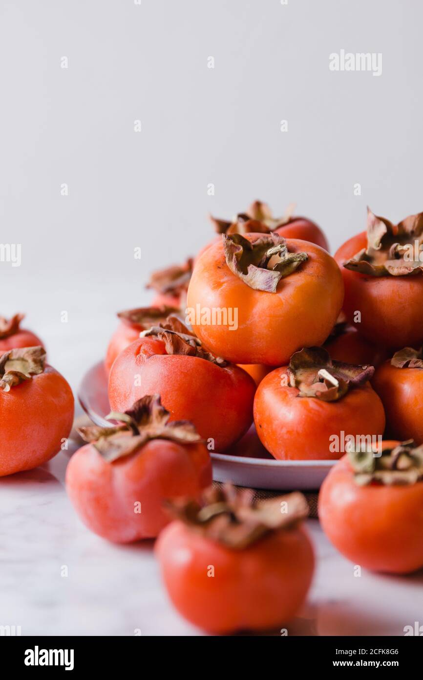 Pila di persimmons freschi su piatto posto su tavola bianca in cucina luminosa Foto Stock