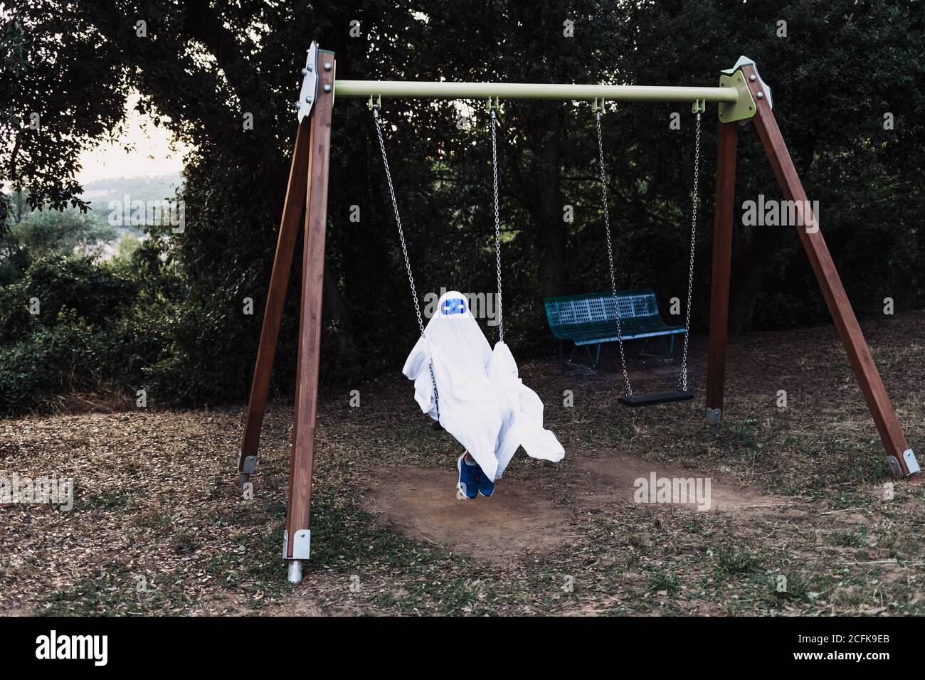 capretto irriconoscibile in costume fantasma bianco che oscilla e gioca sopra Parco giochi durante la vacanza di Halloween Foto Stock