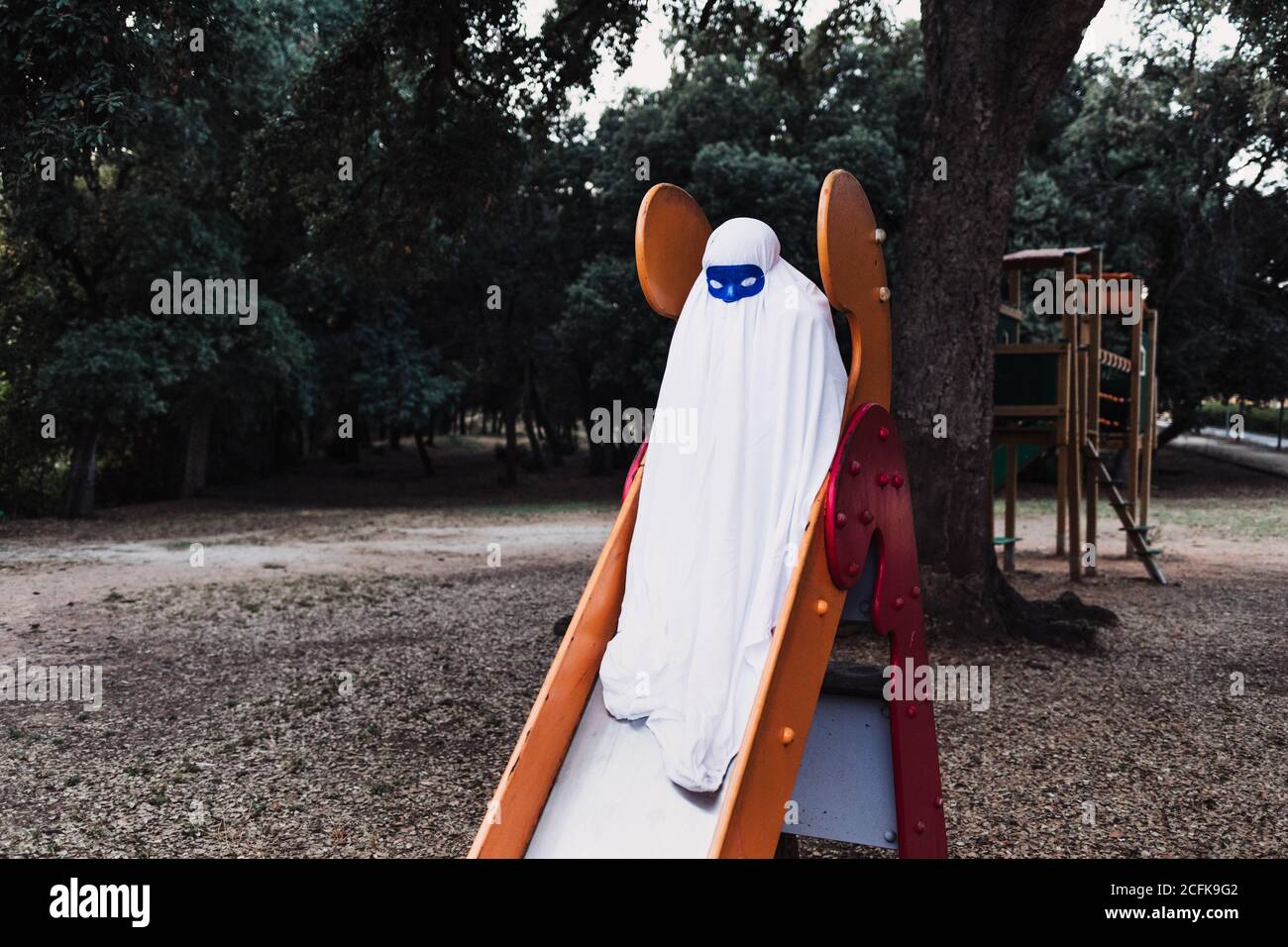 bambino irriconoscibile che indossa maschera e costume fantasma che scivola sul vetrino Durante la celebrazione di Halloween Foto Stock
