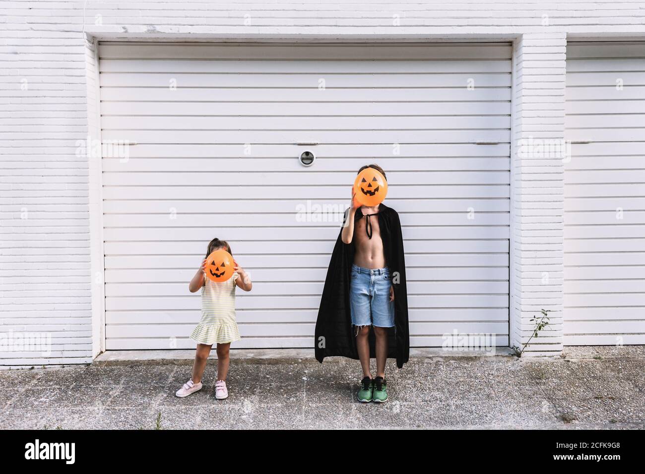 ragazzo e ragazza che ricoprono i volti con palloncini a forma di zucca spaventosa mentre si trovano insieme sulla strada durante il giorno Foto Stock