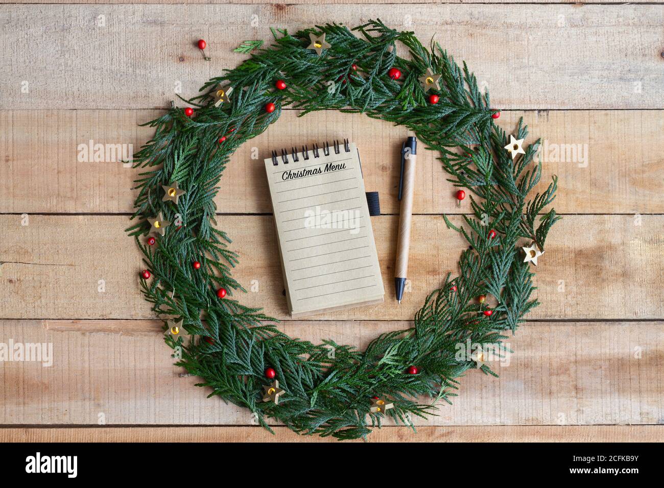 Vista dall'alto della penna per scrivere il menu festivo nel notebook Posto all'interno della corona di Natale su un tavolo di legno Foto Stock