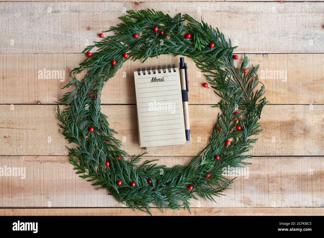 Vista dall'alto della penna per scrivere il menu festivo nel notebook Posto all'interno della corona di Natale su un tavolo di legno Foto Stock