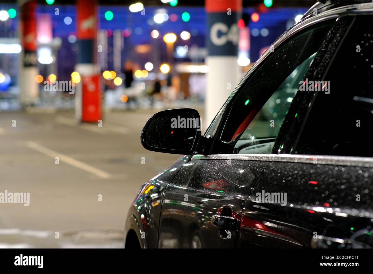 Lo specchietto laterale della vettura è coperto da gocce di pioggia. L'auto è parcheggiata in un angolo buio del parcheggio Foto Stock
