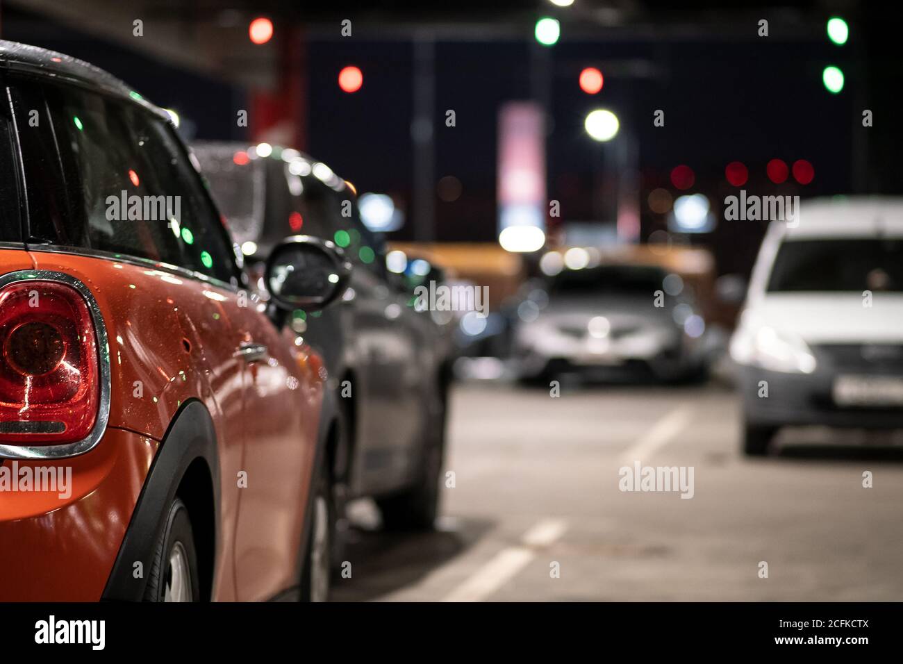 Sfondo, sfocatura, messa a fuoco, bokeh. Lo specchietto laterale della vettura è coperto da gocce di pioggia. L'auto è parcheggiata in un angolo buio del parcheggio Foto Stock