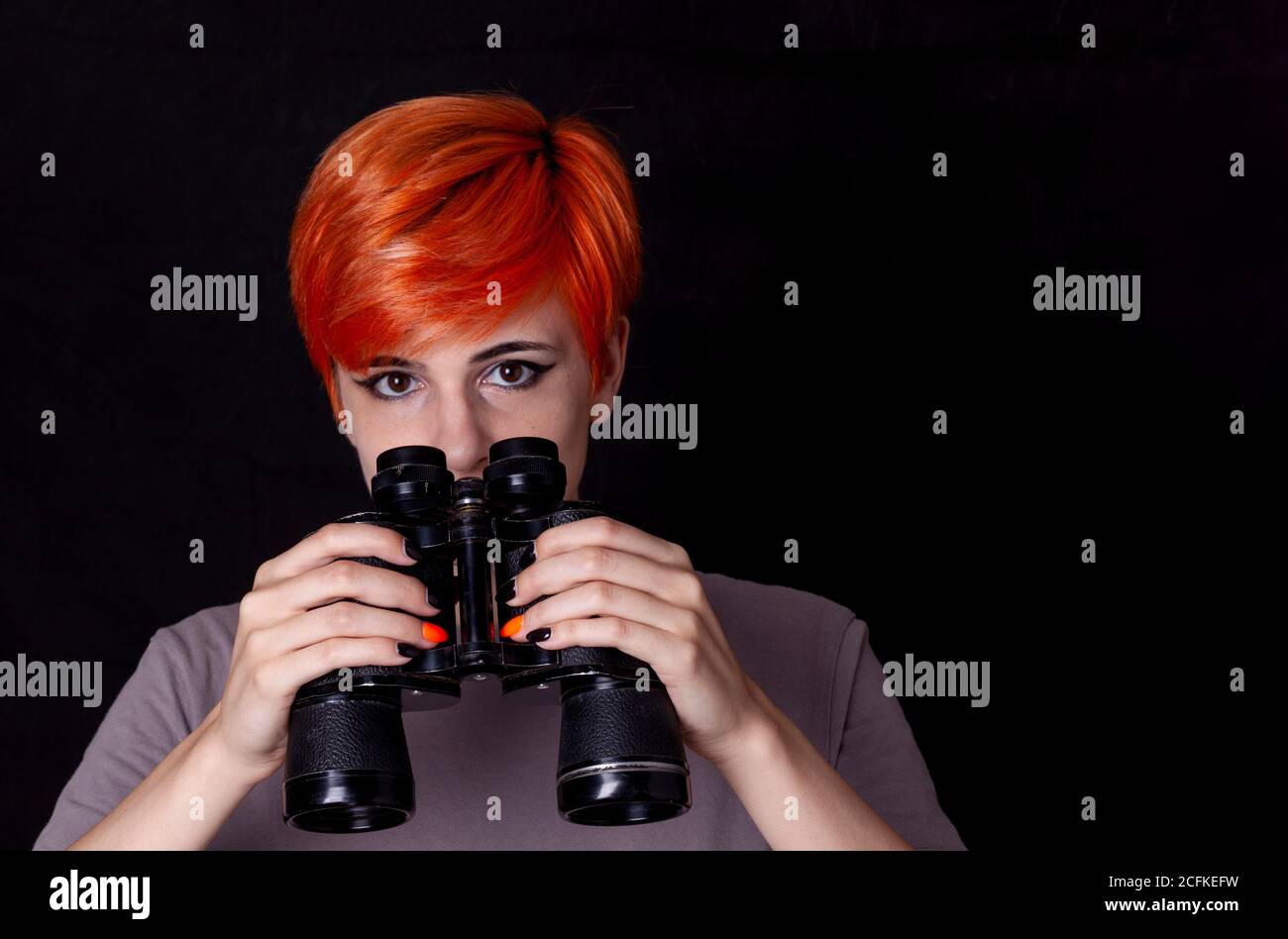 Giovane donna che guarda attraverso binocoli isolati su sfondo nero Foto Stock