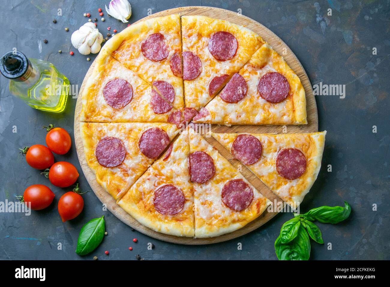Gustosa pizza ai peperoni e ingredienti per la cottura pomodori basilico su fondo in cemento nero. Vista dall'alto della pizza ai peperoni caldi Foto Stock