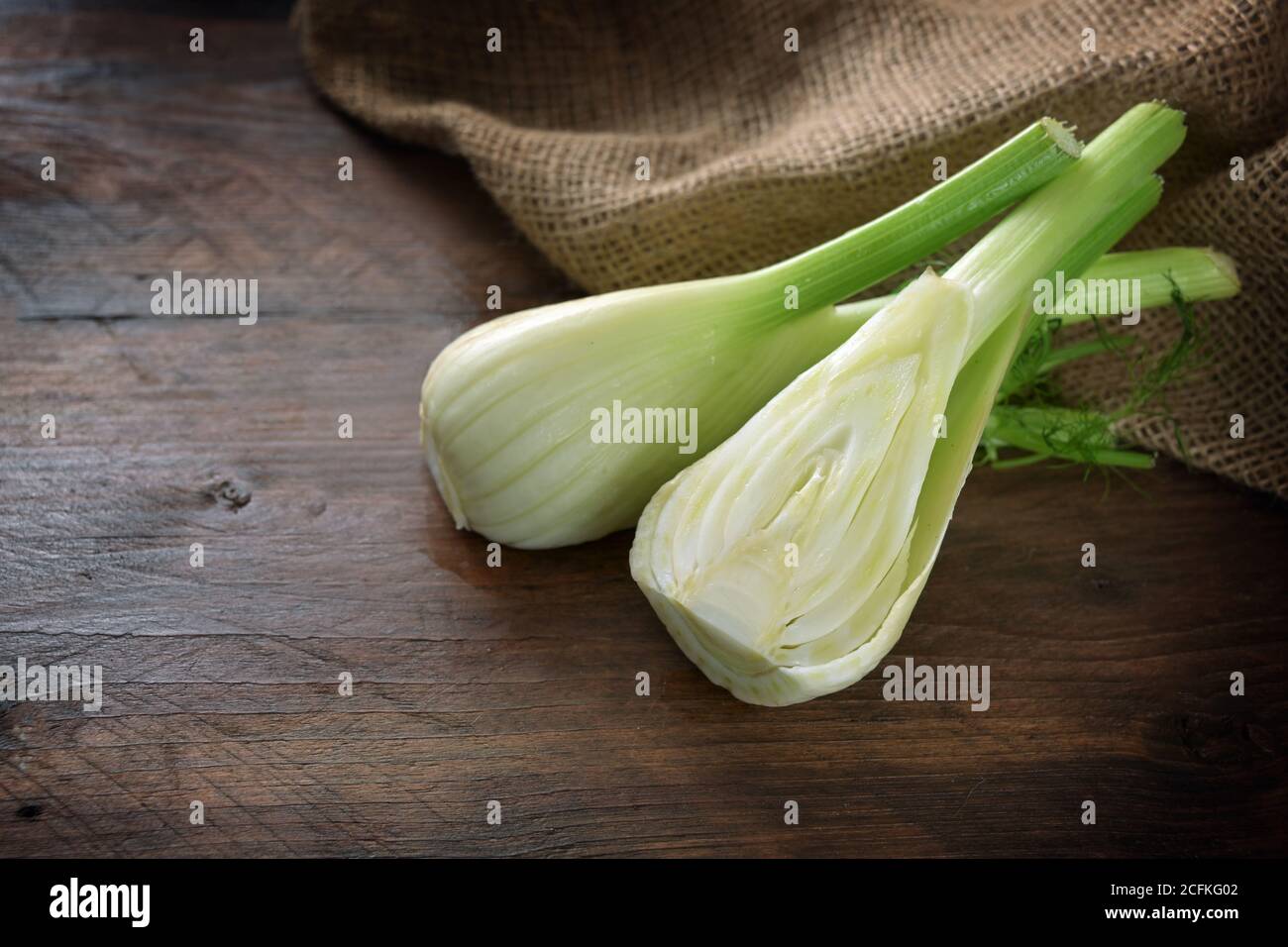 Bulbo di finocchio grezzo dimezzato su un tavolo di legno rustico scuro, verdure mediterranee sane, spazio di copia, fuoco selezionato, profondità di campo stretta Foto Stock