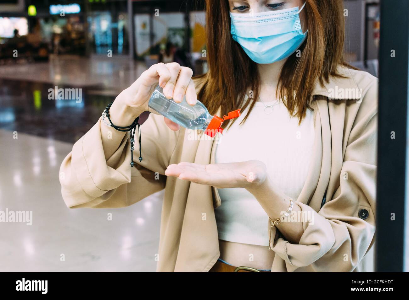 una donna che indossa una maschera facciale e usa gel idroalcolico disinfettare le mani alla stazione ferroviaria Foto Stock