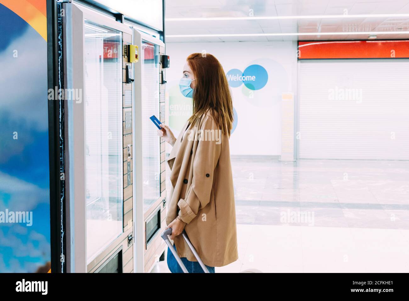 donna con una maschera facciale usa la sua carta di credito a. paga al distributore automatico Foto Stock